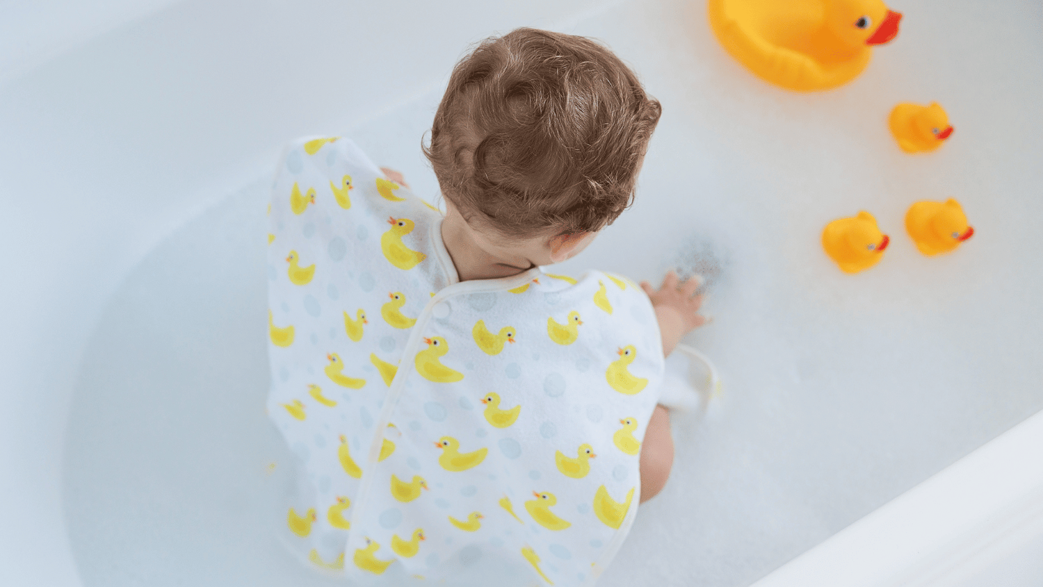 Yellow duck bath towel, bath ducks floating in warm bubble bath, child playing with yellow bath ducks